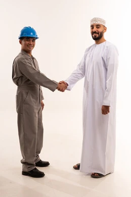 رجل أعمال عُماني وعامل صناعي يتصافحان