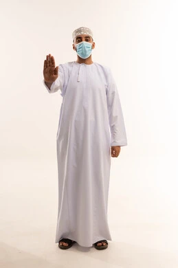 رجل عماني بالزي التقليدي والكمامة يشير بالتوقف
