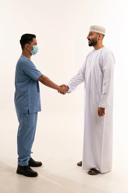 رجل عماني يصافح طبيب يرتدي الزي الطبي الأزرق في الاستوديو