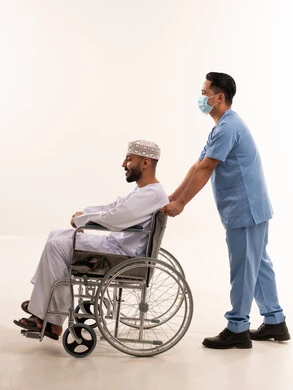 رجل عماني على كرسي متحرك مع ممرض خلفية بيضاء