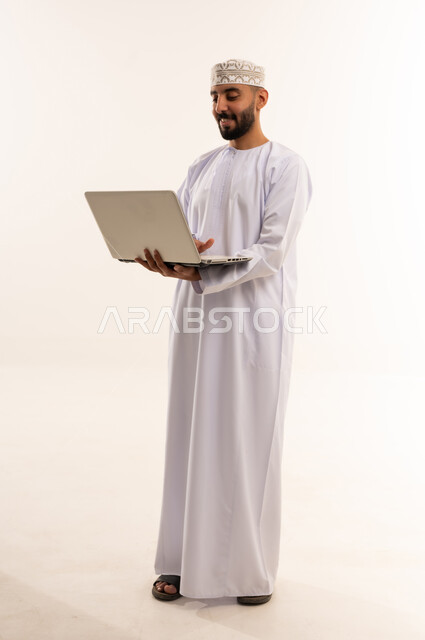 رجل عُماني بالزي التقليدي والدشداشة يستخدم الحاسوب المحمول