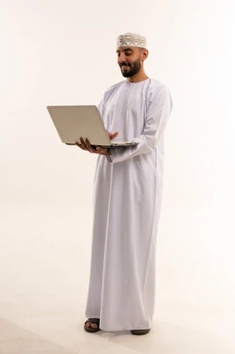 رجل عُماني بالزي التقليدي والدشداشة يستخدم الحاسوب المحمول