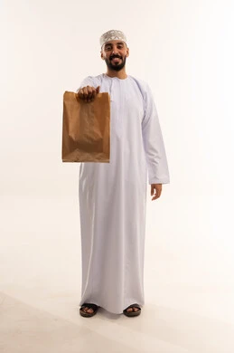 رجل عُماني يحمل كيس تسوق ورقي بخلفية بيضاء