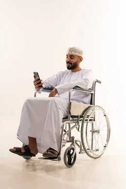 رجل عماني على كرسي متحرك يستخدم الجوال خلفية بيضاء