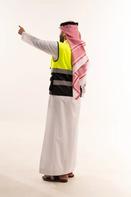 رجل سعودي يرتدي سترة سلامة ويشير على خلفية بيضاء