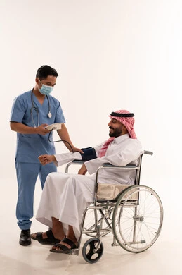 ممرض يقيس ضغط دم مريض سعودي على كرسي متحرك
