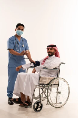 ممرض يقيس ضغط دم مريض سعودي على كرسي متحرك