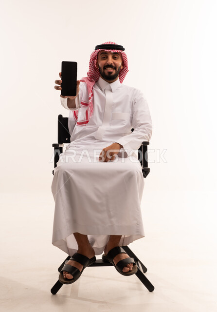 رجل سعودي بالثوب يحمل هاتفاً ذكياً في الاستوديو