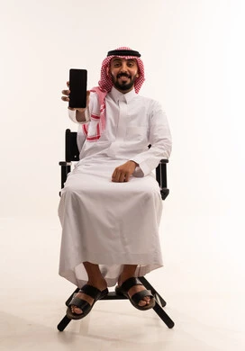 رجل سعودي بالثوب يحمل هاتفاً ذكياً في الاستوديو