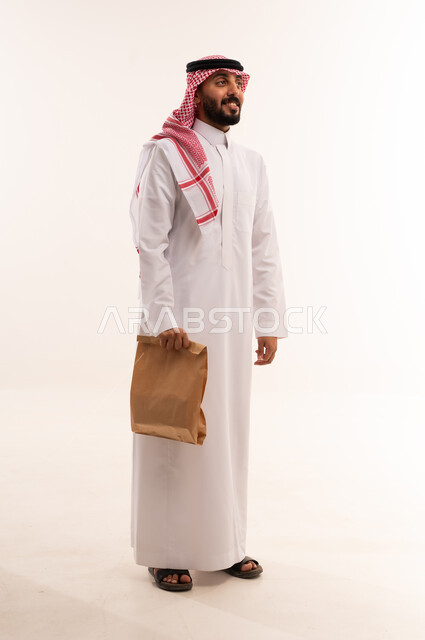رجل سعودي بالزي التقليدي يحمل كيساً ورقياً