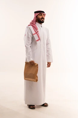 رجل سعودي بالزي التقليدي يحمل كيساً ورقياً