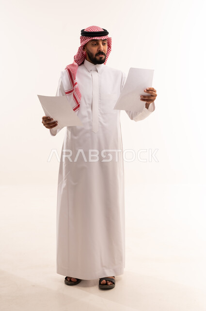 رجل سعودي يقرأ مستندات عمل على خلفية بيضاء