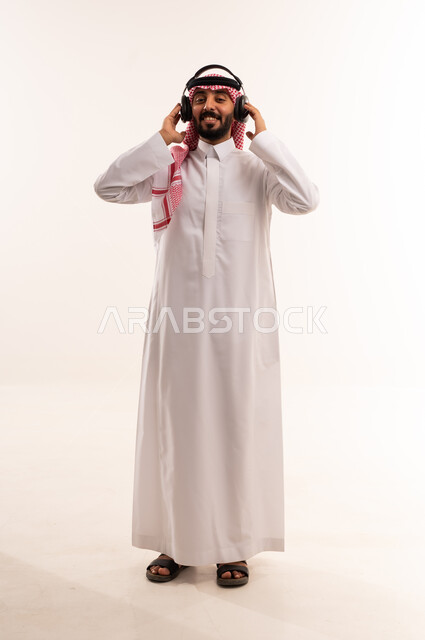 رجل سعودي بالثوب يرتدي سماعات رأس على خلفية بيضاء