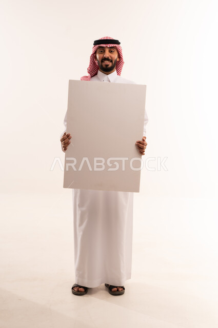 رجل سعودي يحمل لوحة بيضاء فارغة في استوديو