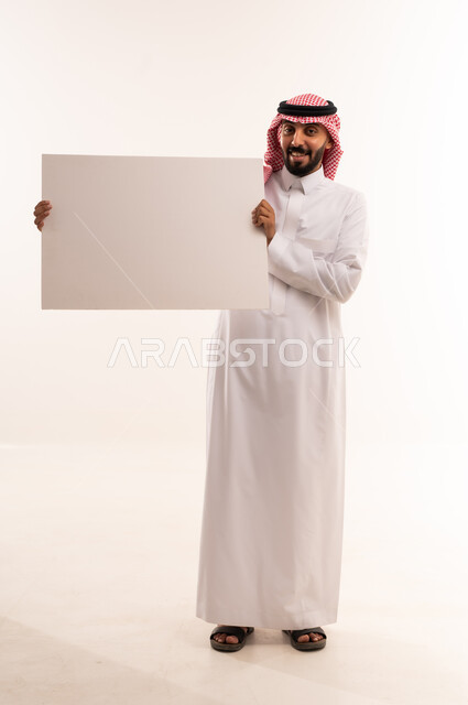 رجل سعودي بالزي التقليدي يحمل لوحة إعلانية بيضاء فارغة