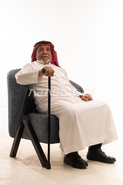 رجل سعودي مسن يجلس على كرسي مع عصا مشي