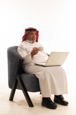 رجل سعودي مسن مع كمبيوتر محمول وفنجان قهوة