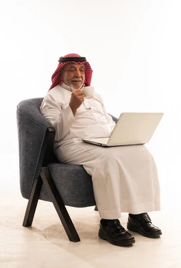 Elderly Saudi Man Using Laptop and Drinking Coffee