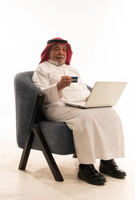 Saudi Senior Using Laptop and Credit Card on White Background