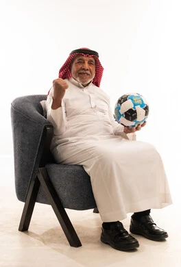 رجل سعودي مسن بالزي التقليدي ممسكاً بكرة قدم