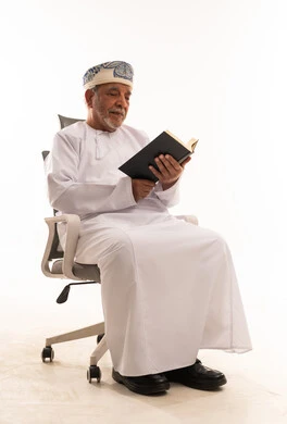 رجل عُماني مسن يقرأ كتاباً على كرسي مكتب