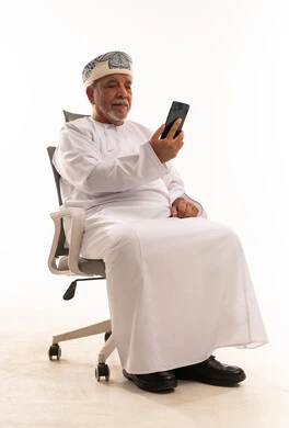 Elderly Omani Man in Traditional Dress Using Smartphone