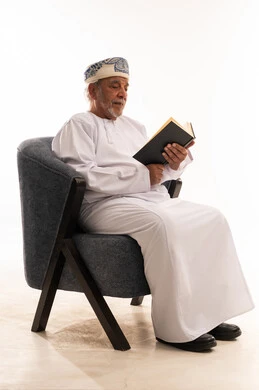 رجل عُماني مسن يقرأ كتاباً بالزي التقليدي