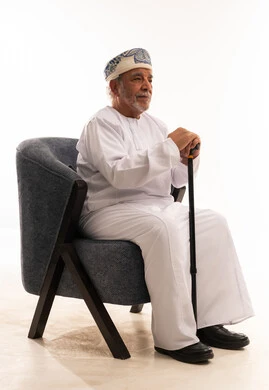 رجل عُماني مسن يرتدي كمة ويجلس مع عصا مشي في استوديو