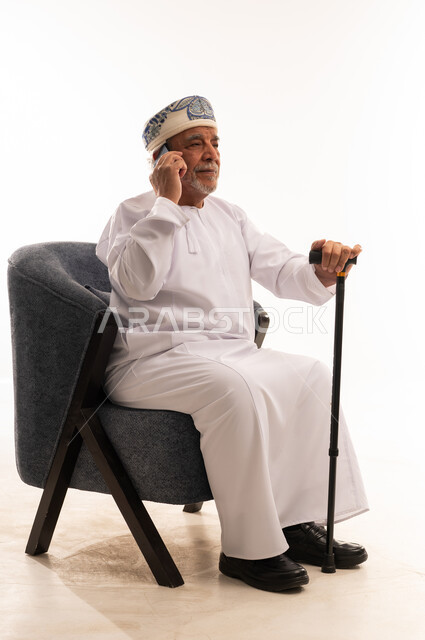 رجل عماني مسن يستخدم الهاتف المحمول مع عصا مشي