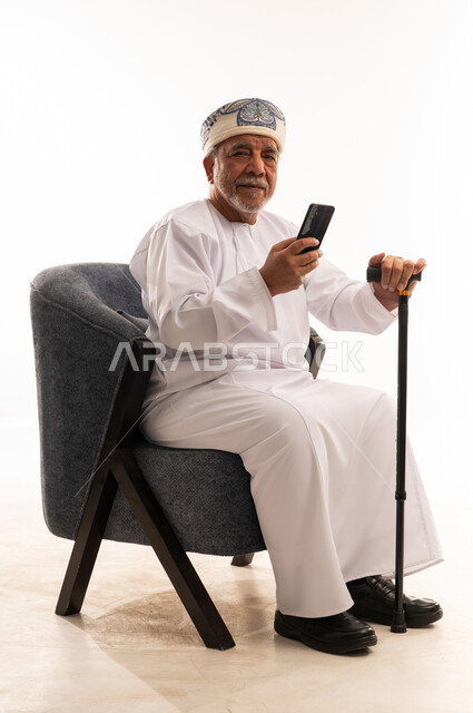 رجل عماني مسن مع هاتف ذكي وعصا مشي