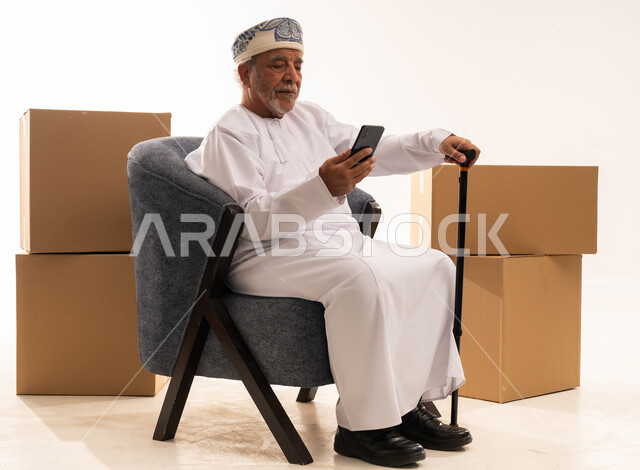 Elderly Omani Man Using Smartphone with Shipping Boxes