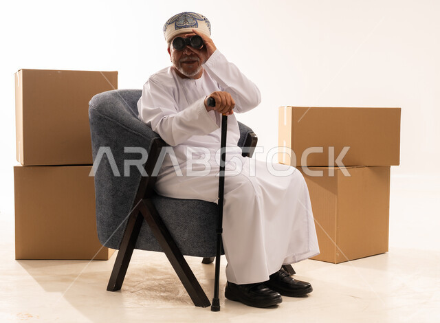 Elderly Omani Man Using Binoculars Near Moving Boxes