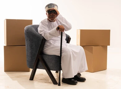 Elderly Omani Man Using Binoculars Near Moving Boxes