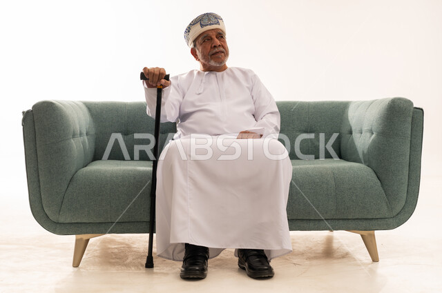 رجل عماني مسن مع عصا مشي على الأريكة