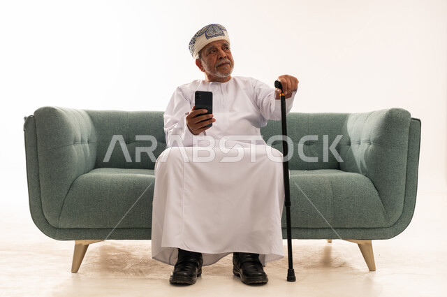 رجل عماني مسن يحمل هاتفا ذكيا وعصا مشي