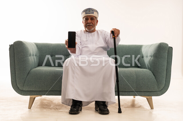 Elderly Omani Man with Smartphone on Sofa