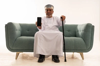 Elderly Omani Man with Smartphone on Sofa