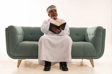Elderly Omani Man Reading Book on Sofa