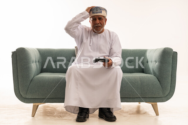 Elderly Omani Man Frustrated Playing Video Games on Sofa