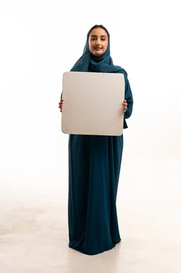 امرأة سعودية بالعباءة تحمل لوحة بيضاء فارغة في الاستوديو