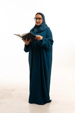 امرأة سعودية بعباءة زرقاء تقرأ كتاباً بخلفية بيضاء