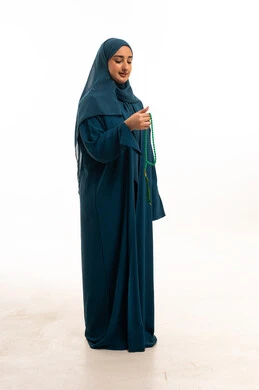 امرأة سعودية بالعباءة تمسك مسبحة في استوديو باللون الأبيض