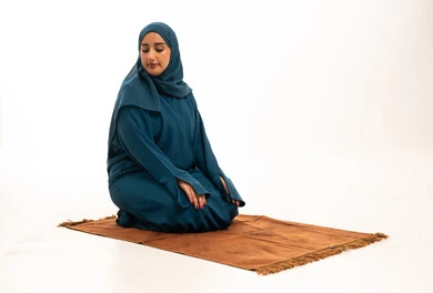 امرأة عربية مسلمة تصلي على سجادة صلاة في استوديو