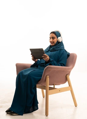 امرأة سعودية بعباءة تستخدم جهاز لوحي مع سماعات