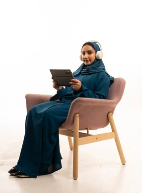 Emirati Woman with Tablet and Headphones in Armchair