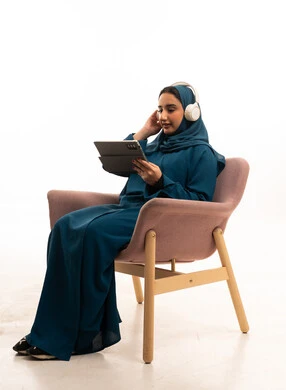 Saudi Woman in Blue Abaya Using Tablet and Headphones