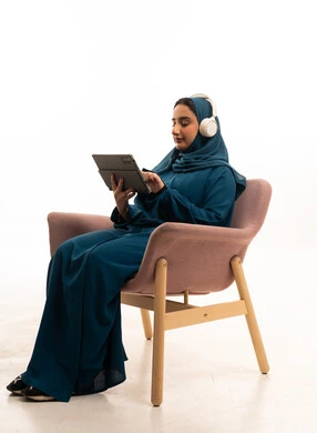 امرأة عربية بالعباءة الزرقاء تستخدم جهاز لوحي وسماعات