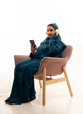 Arab Woman in Teal Abaya Using Headphones and Phone