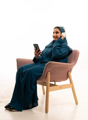 امرأة سعودية بالعباءة ترتدي سماعات وتمسك هاتف