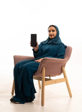 امرأة عربية بعباءة تمسك هاتف ذكي في الاستوديو